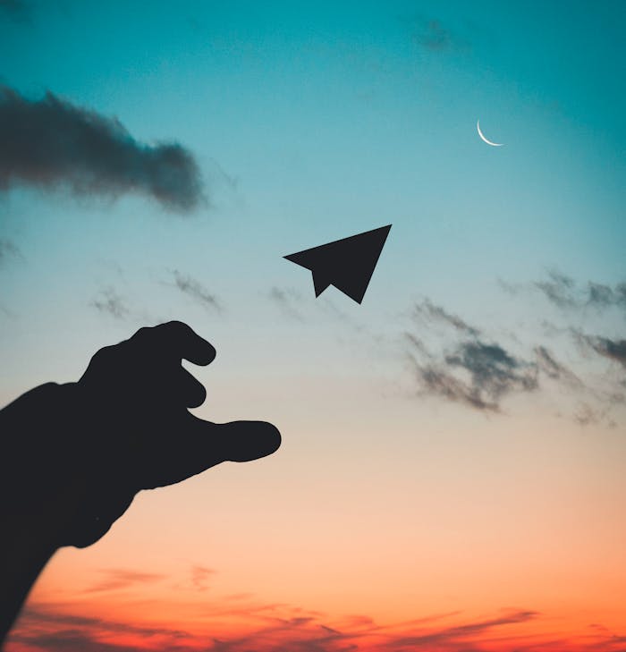 silhouette-photo-of-man-throw-paper-plane-1262304 A silhouette of a hand launching a paper plane against a colorful dusk sky with a crescent moon.
